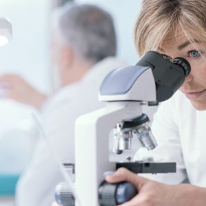 image of a midical lab with a female scientist looking into a microscope with another scientist on the background